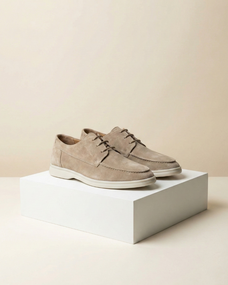 Pair of beige suede loafers on a white platform with a beige background