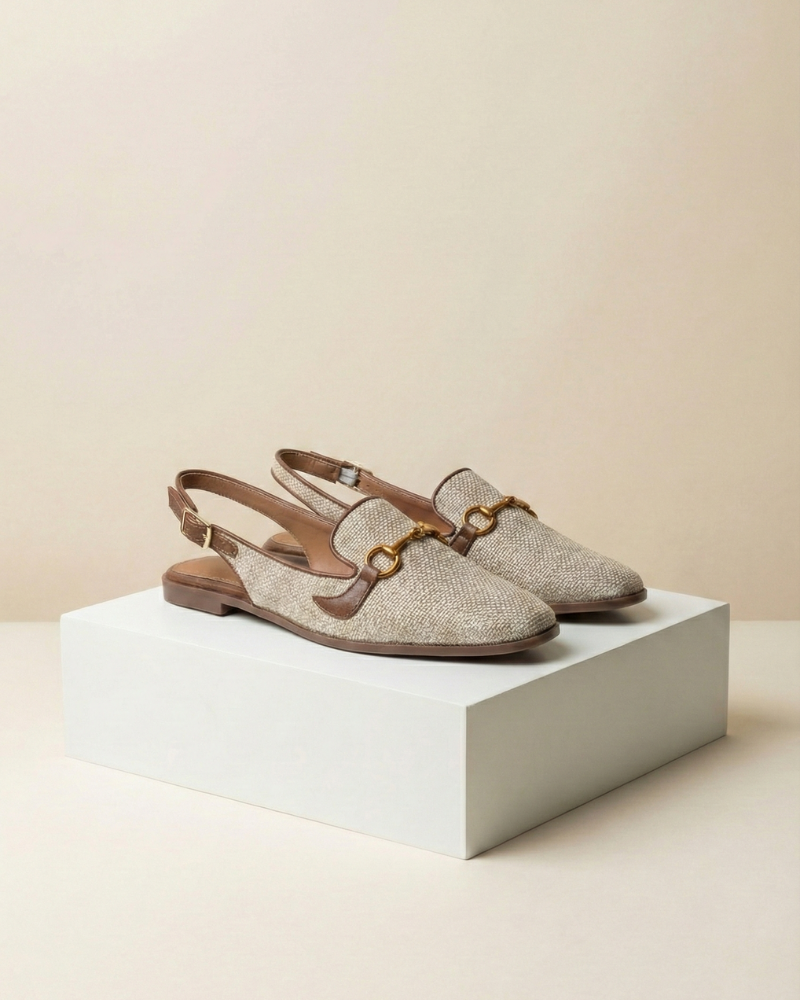 Pair of beige slingback loafers with brown straps on a white platform against a beige background
