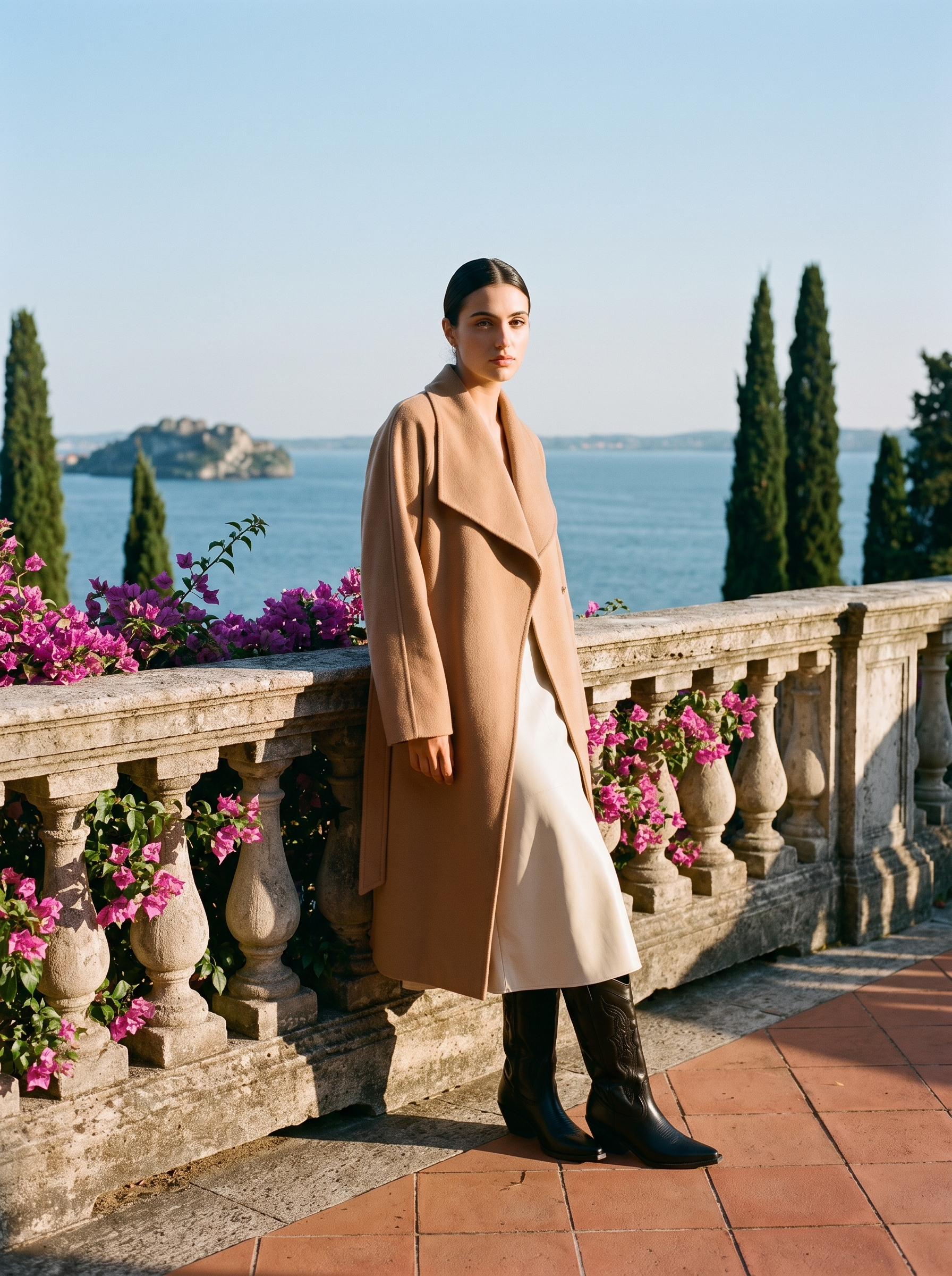 Full body front view of a woman in black pointed toe western knee high boots and a cream skirt on a Lake Como terrace — Aveloire