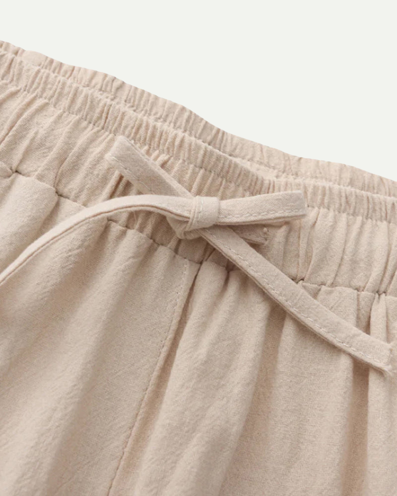 Close-up of beige pants with a tie waist on a light gray background