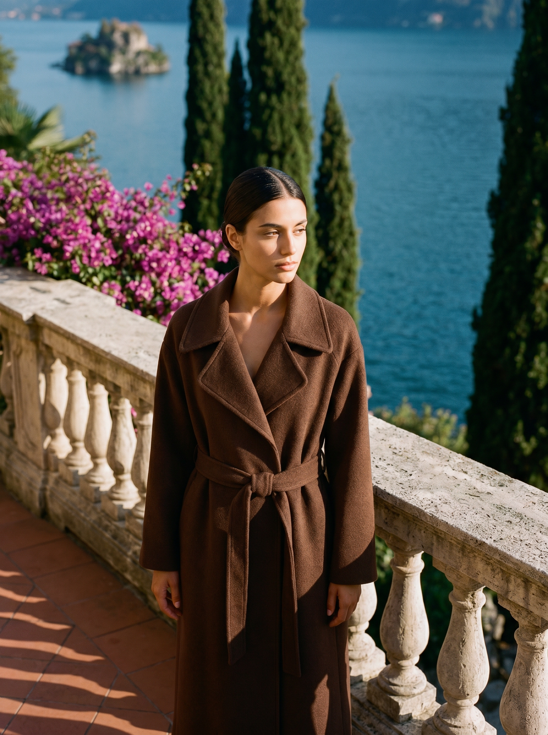 Woman wearing chocolate brown belted wool wrap coat on a Lake Como terrace