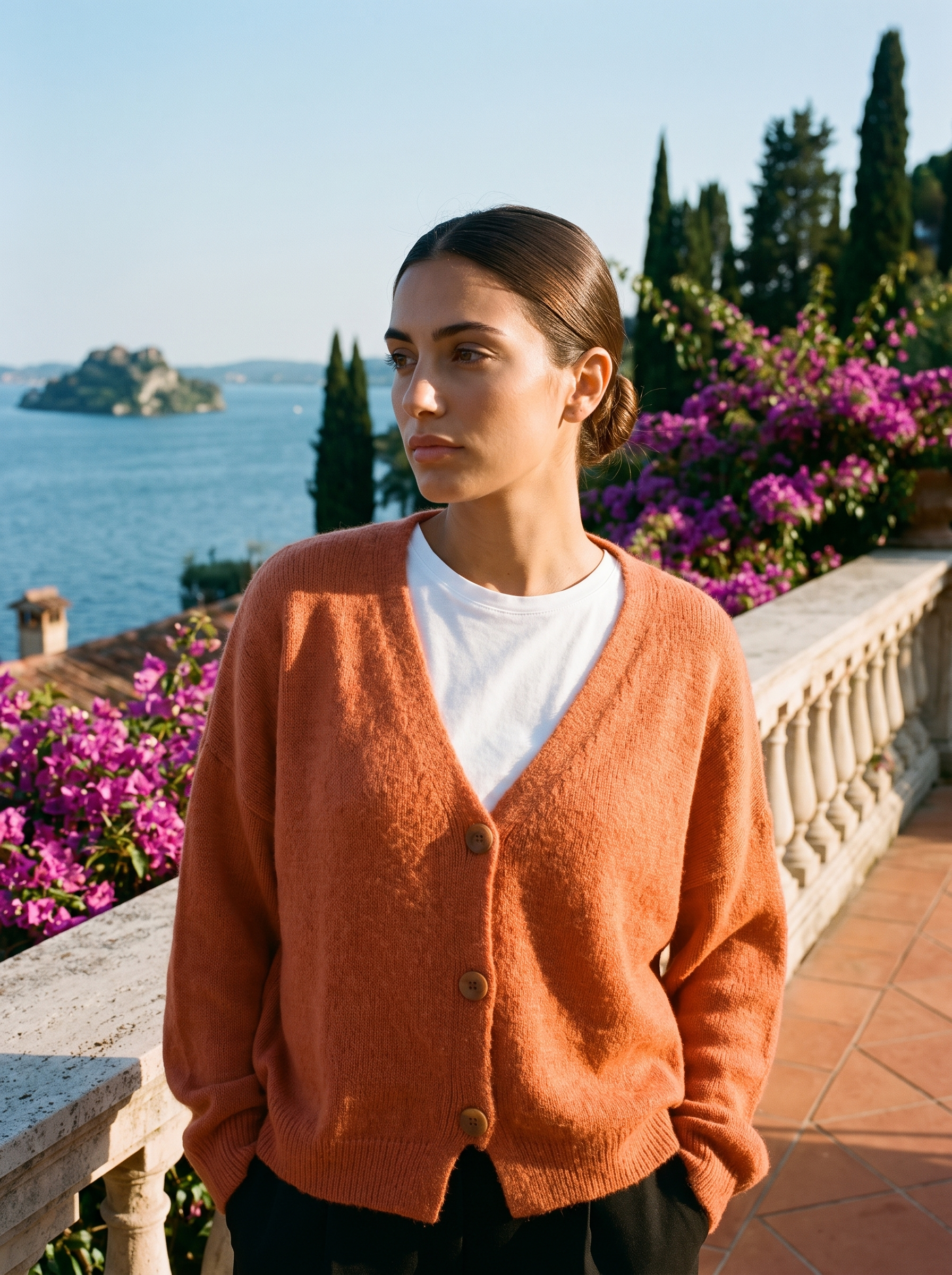 Woman wearing an orange V-neck cardigan on a terrace overlooking Lake Como, old money style — Aveloire