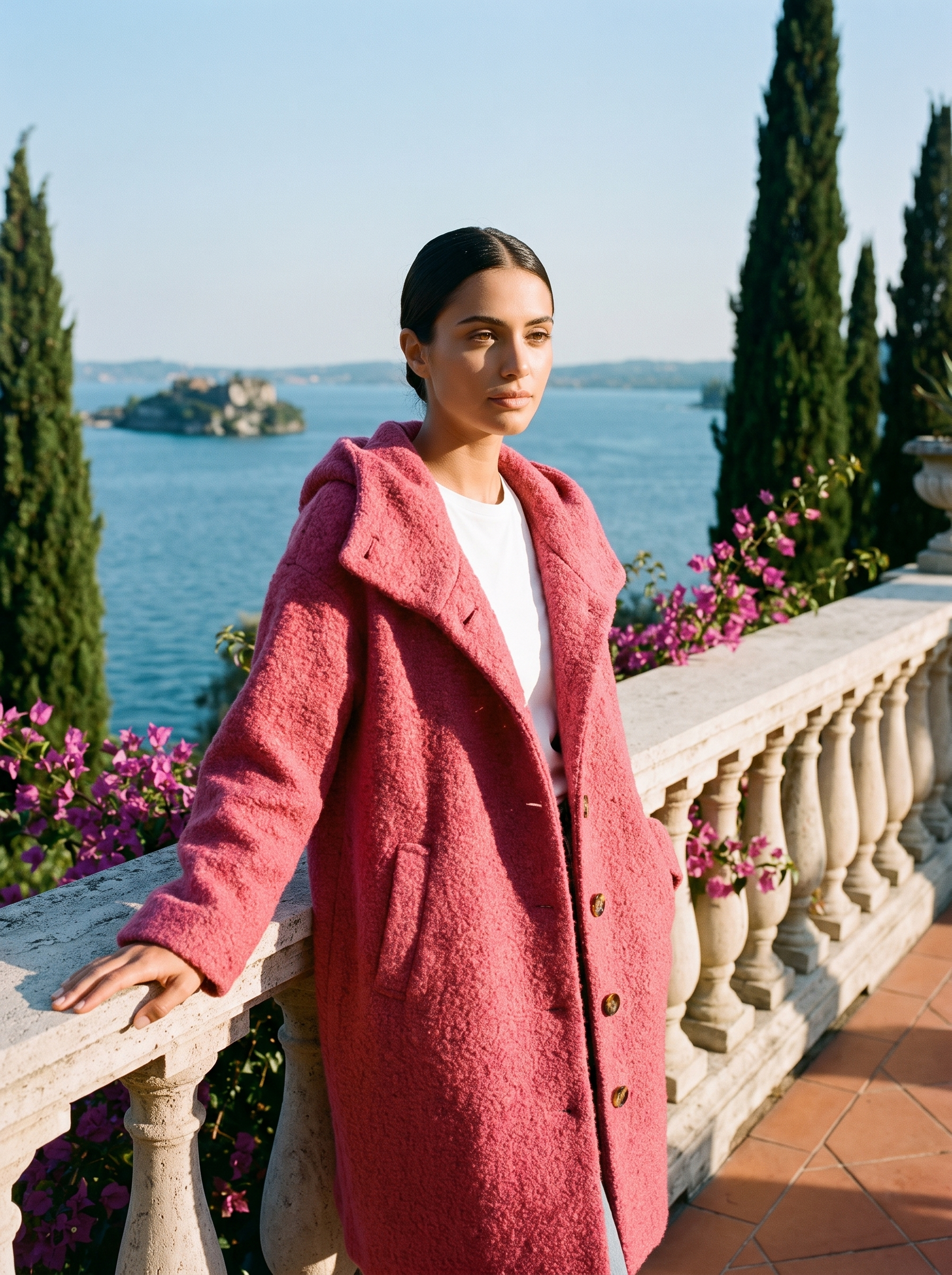 Woman wearing a raspberry pink hooded wool coat on a terrace overlooking Lake Como — Aveloire