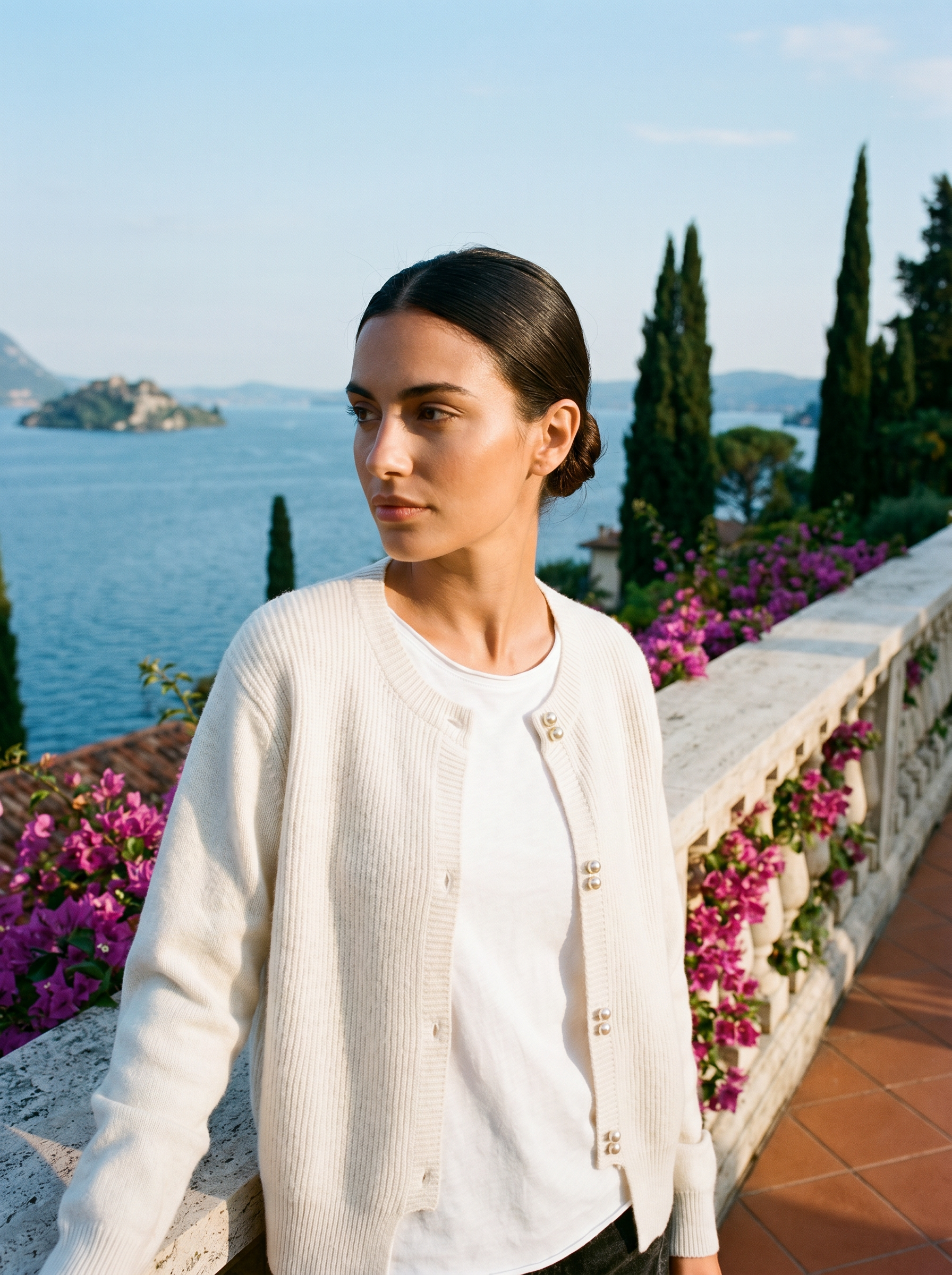 Woman wearing a white round-neck cardigan on a terrace overlooking Lake Como, old money style — Aveloire