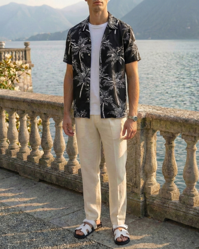 Men’s black Hawaiian short sleeve shirt with palm print styled with light trousers