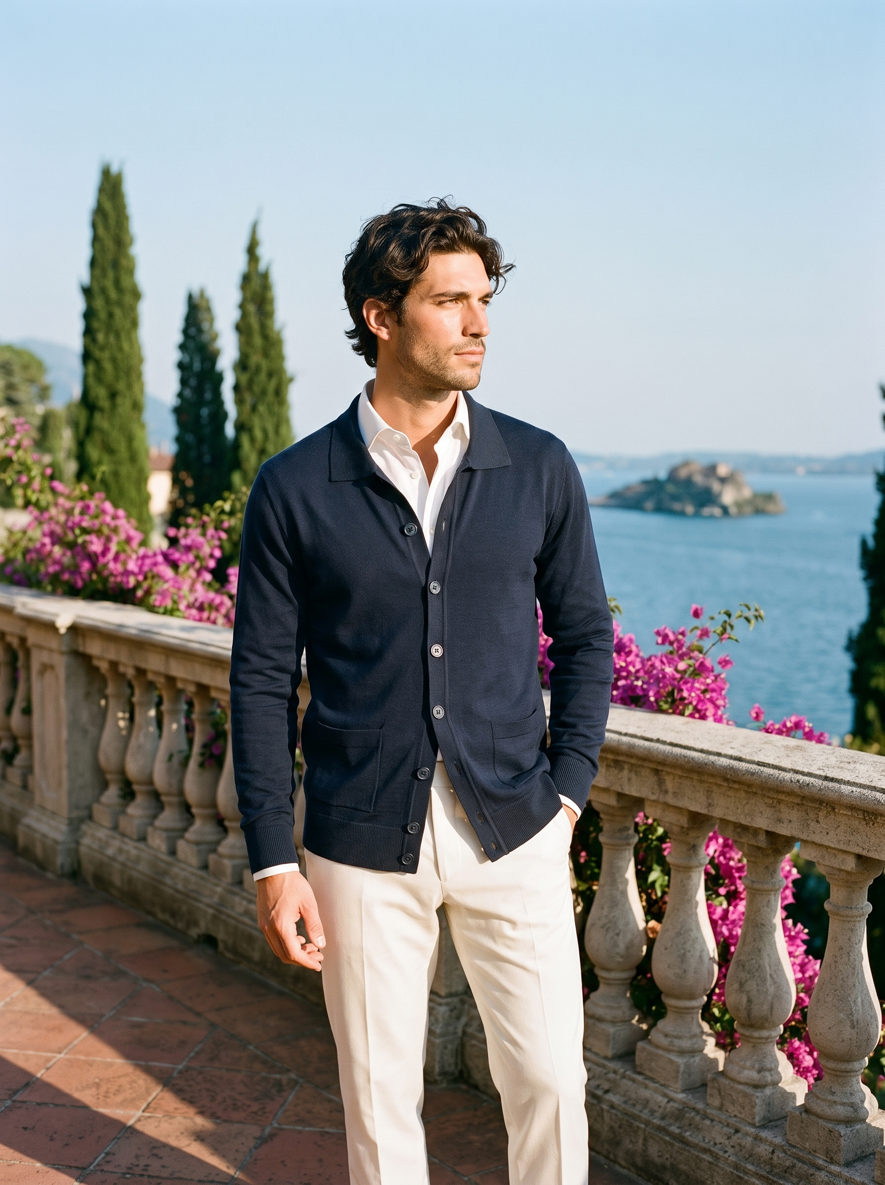 Full body view of a man in a navy button-up collared cardigan and cream trousers on a Lake Como terrace — Aveloire