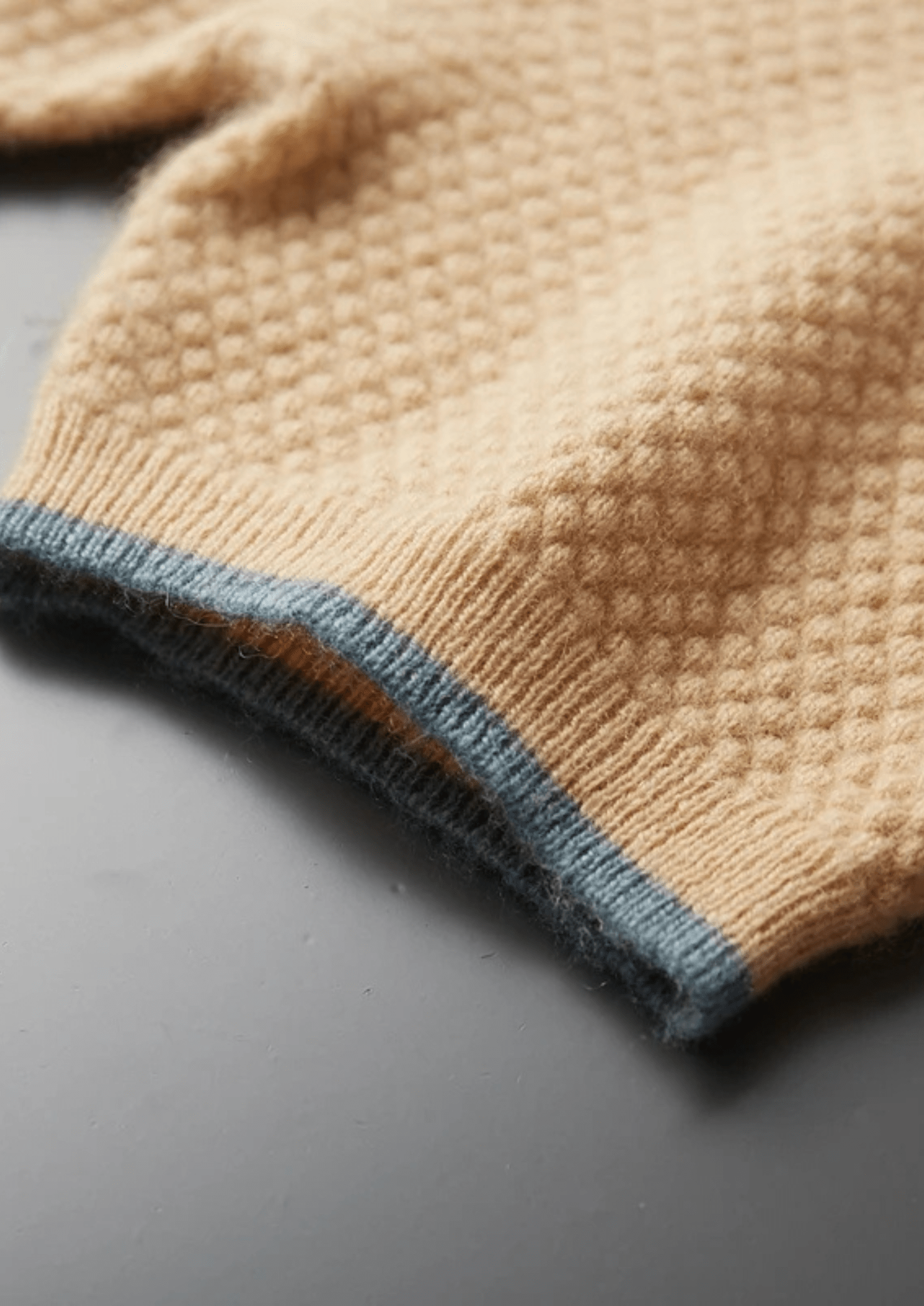 Close-up of a beige knitted sweater with blue trim on a gray surface