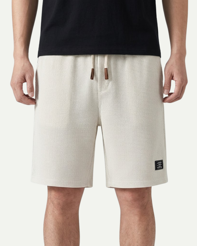 Person wearing white waffle shorts with a black logo on a white background