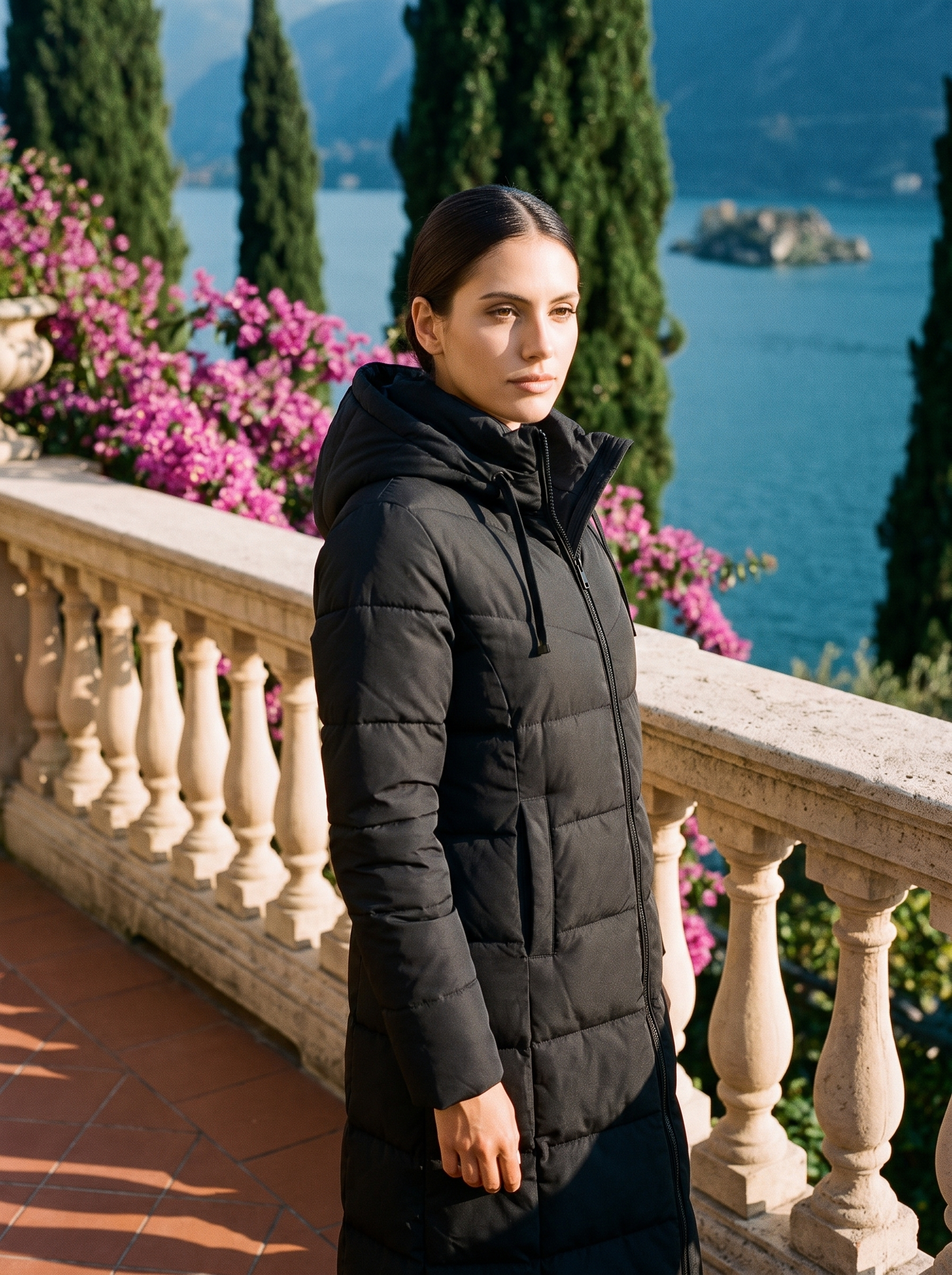 Woman wearing black longline hooded puffer coat on a Lake Como terrace