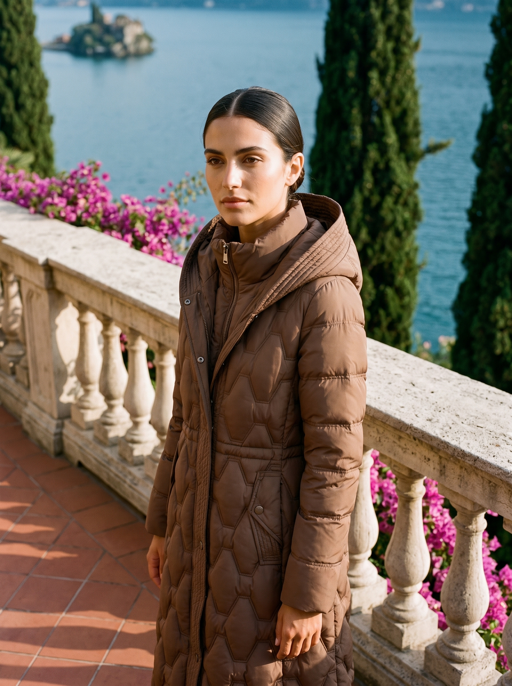 Woman wearing mocha brown onion-quilted longline hooded puffer coat on a Lake Como terrace